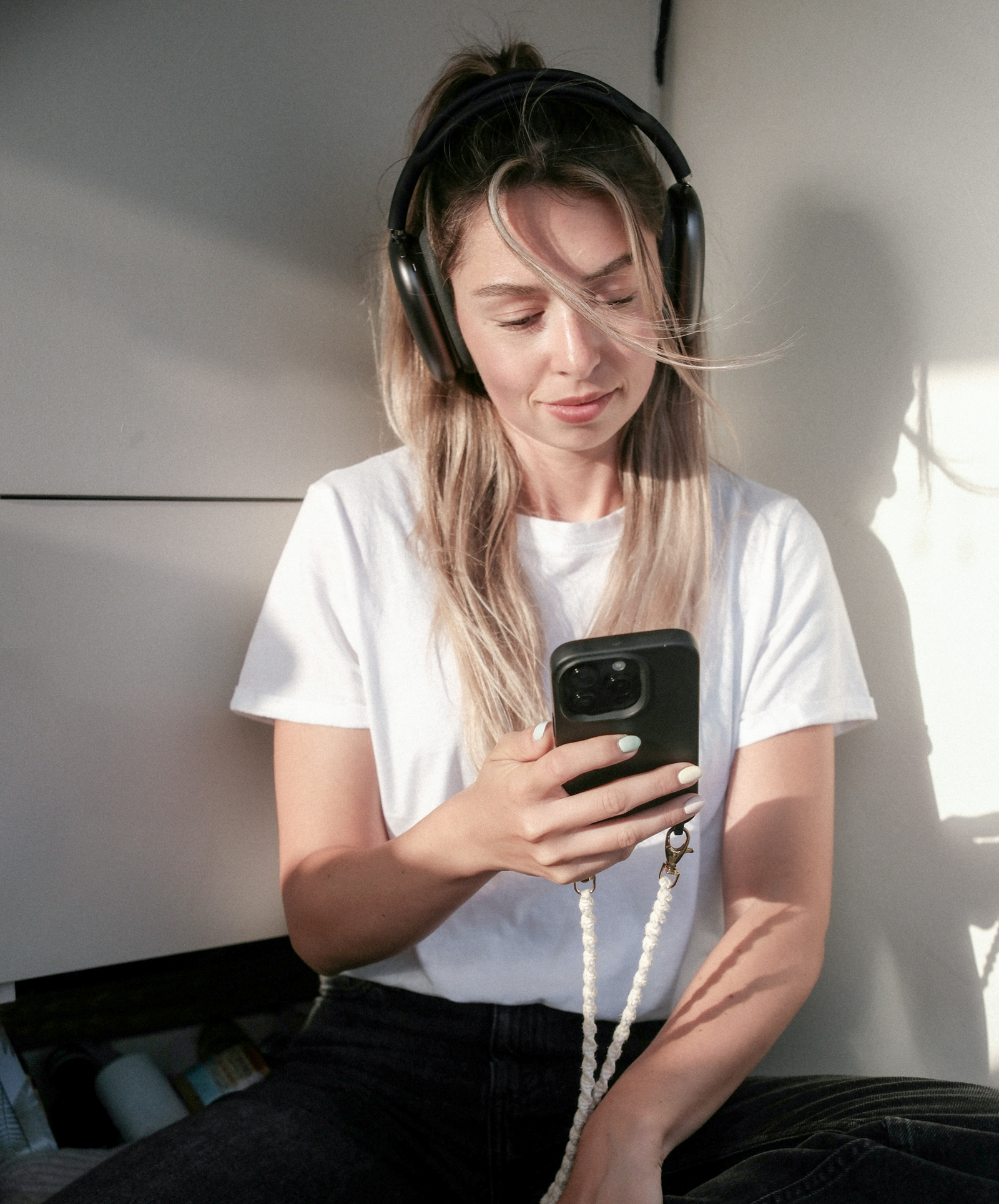 Junge Frau mit Kopfhörern schaut auf ihr Smartphone und nutzt ChatGPT möglicherweise für ein Coaching.