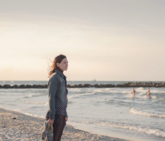 Frau steht nachdenklich am Meer und blickt in die Ferne.