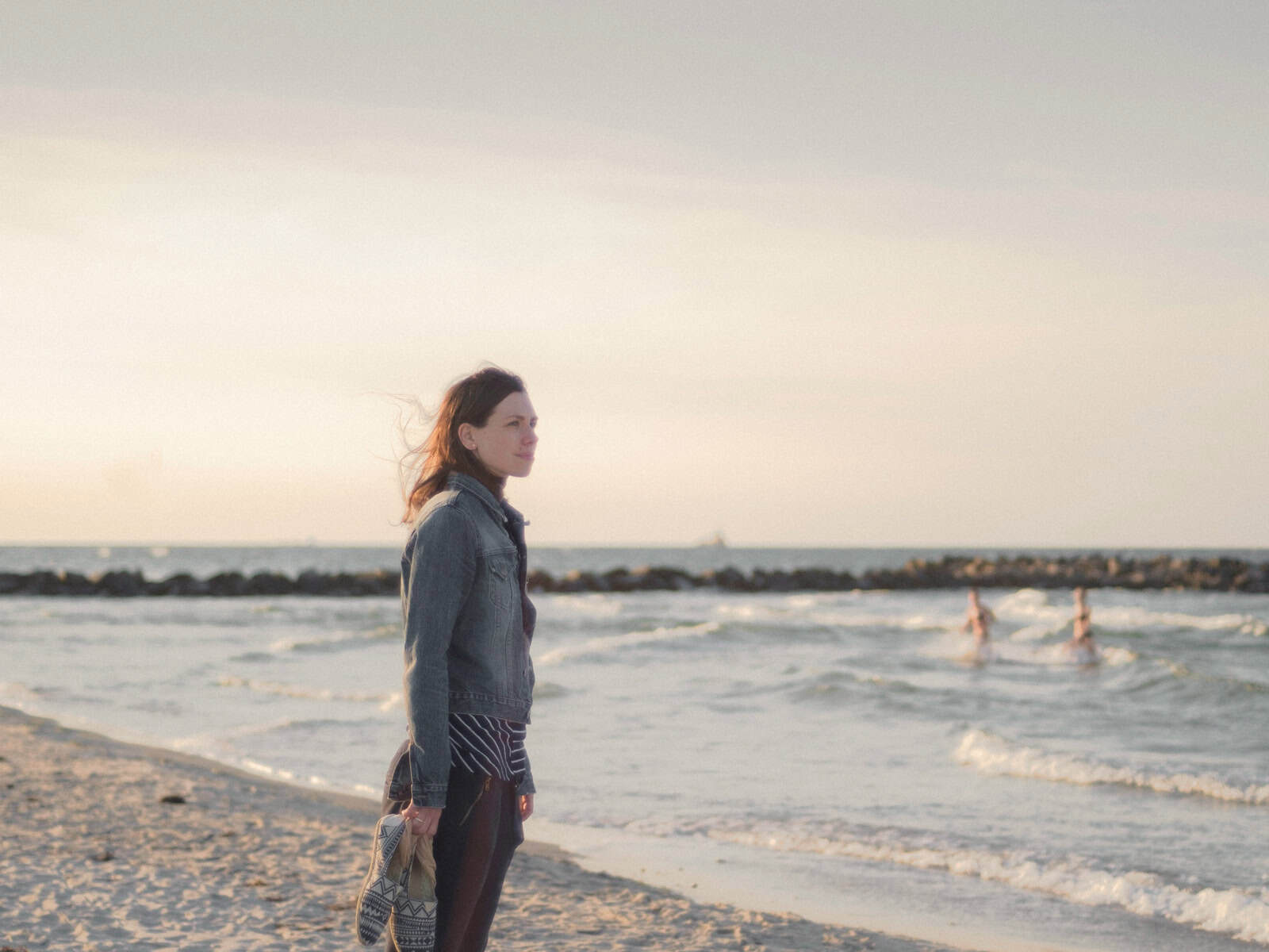 Frau steht nachdenklich am Meer und blickt in die Ferne.