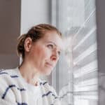Frau blickt nachdenklich aus dem Fenster; Symbolbild für einen Erfahrungsbericht über eine Schamanin und spirituelle Angebote.