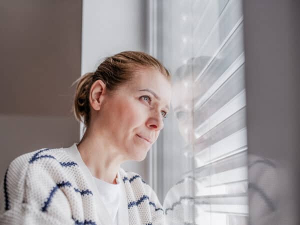 Frau blickt nachdenklich aus dem Fenster; Symbolbild für einen Erfahrungsbericht über eine Schamanin und spirituelle Angebote.
