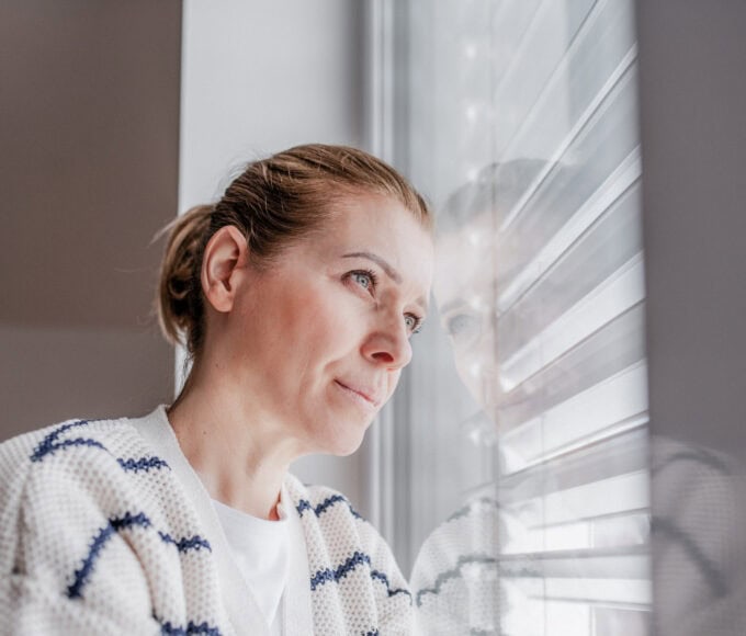 Frau blickt nachdenklich aus dem Fenster; Symbolbild für einen Erfahrungsbericht über eine Schamanin und spirituelle Angebote.