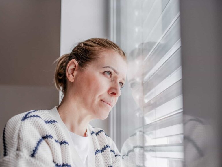 Frau blickt nachdenklich aus dem Fenster; Symbolbild für einen Erfahrungsbericht über eine Schamanin und spirituelle Angebote.
