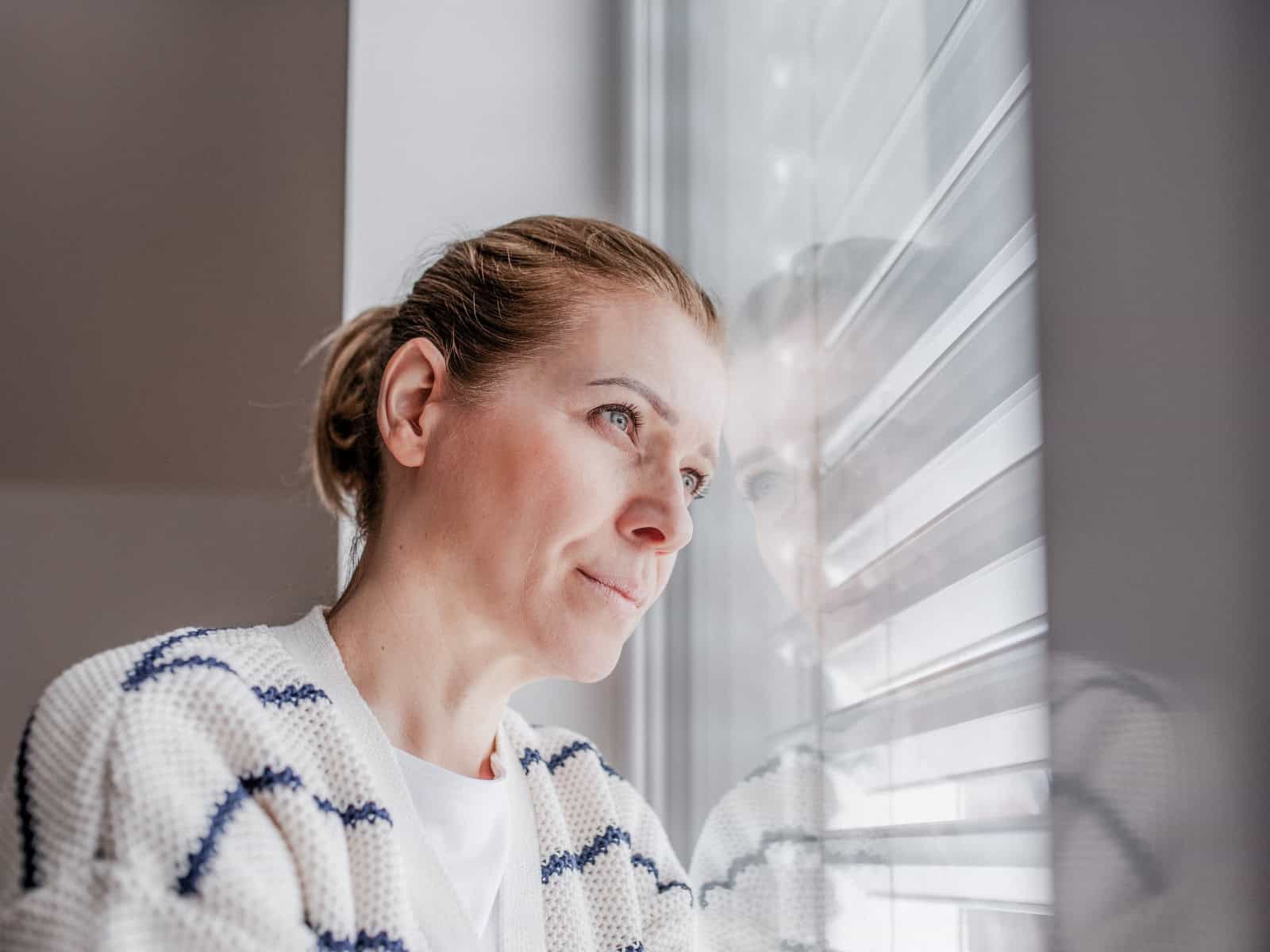 Frau blickt nachdenklich aus dem Fenster; Symbolbild für einen Erfahrungsbericht über eine Schamanin und spirituelle Angebote.