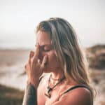 Frau mit geschlossenen Augen berührt mit zwei Fingern ihre Stirn; das Bild steht symbolisch für den Mythos um Zirbeldrüse, Stirnchakra und „drittes Auge“.