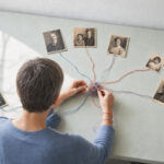Person entwirrt farbige Fäden zwischen alten Familienfotos – Symbolbild zur Kritik an Ahnenheilung.