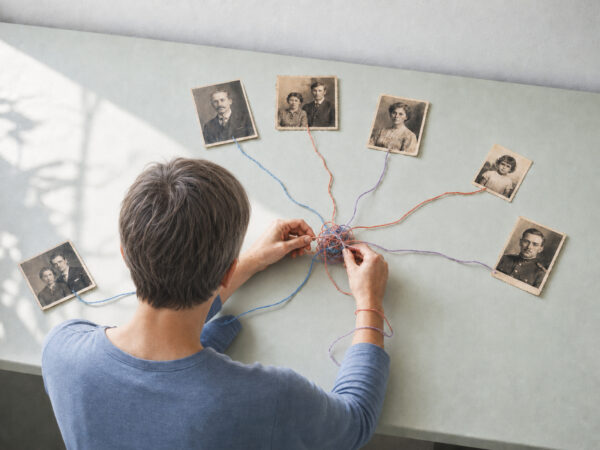 Person entwirrt farbige Fäden zwischen alten Familienfotos – Symbolbild zur Kritik an Ahnenheilung.
