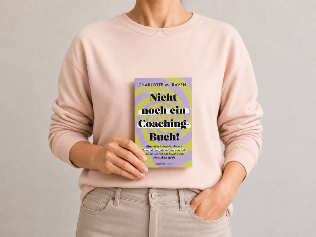 Frau im violetten Pullover hält das Buch „Nicht noch ein Coaching-Buch!“ von Charlotte M. Raven vor neutralem Hintergrund in der Hand.
