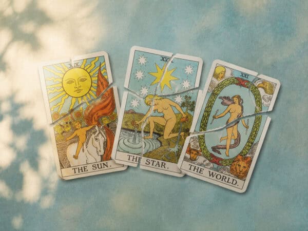 Drei zerrissene Tarotkarten mit den Motiven Sonne, Stern und Welt liegen nebeneinander auf einer farbigen Oberfläche.