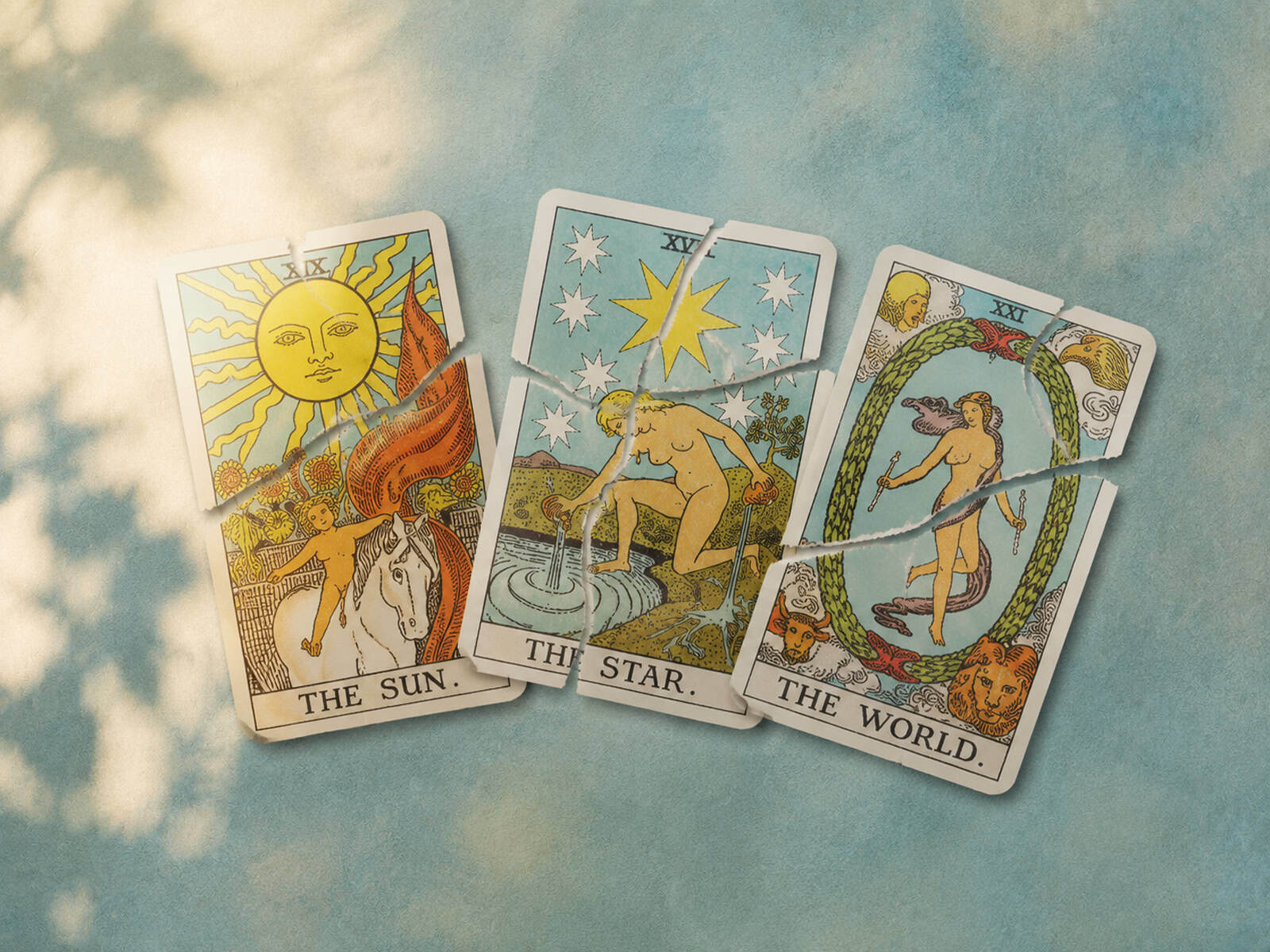 Drei zerrissene Tarotkarten mit den Motiven Sonne, Stern und Welt liegen nebeneinander auf einer farbigen Oberfläche.