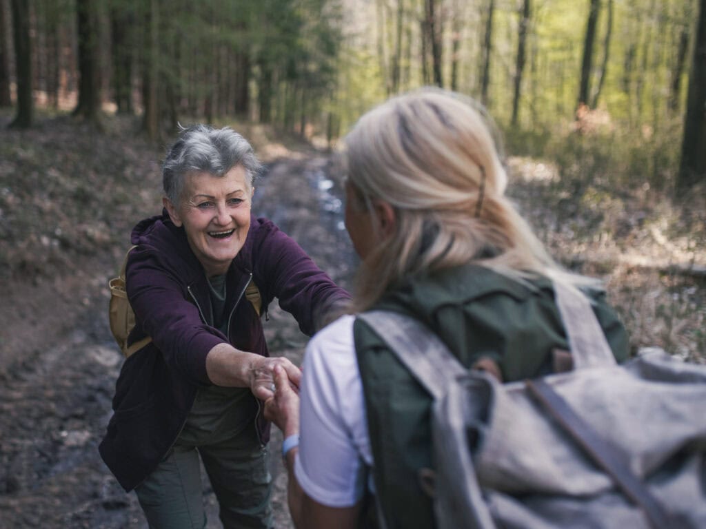 Klassische Spiritualität: Zwei Frauen unterstützen sich bei einer gemeinsamen Wanderung im Wald