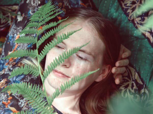 Klassische Spiritualität: Junge Frau erlebt einen ruhigen Moment zwischen Farnen in der Natur