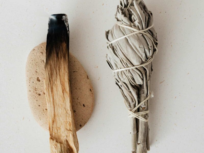 Räuchern mit weißem Salbei und Palo Santo auf hellem Stoffuntergrund