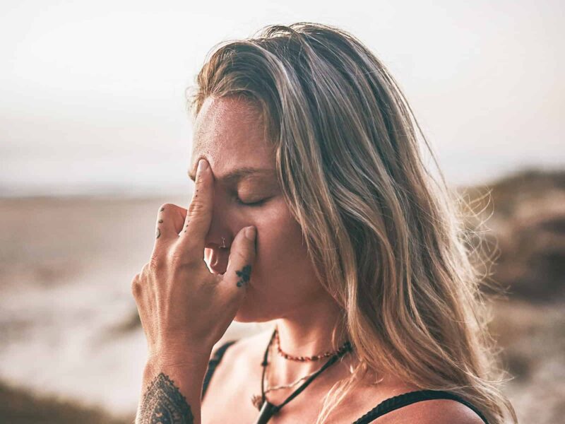 Frau mit geschlossenen Augen berührt mit zwei Fingern ihre Stirn; das Bild steht symbolisch für den Mythos um Zirbeldrüse, Stirnchakra und „drittes Auge“.