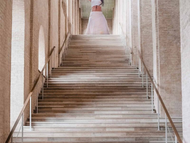 Frau in weißer Kleidung steht mit ausgebreiteten Armen am oberen Ende einer großen Treppe – Symbolbild zum Thema „Junge seelen, Alte seelen“ und spirituelle Hierarchien